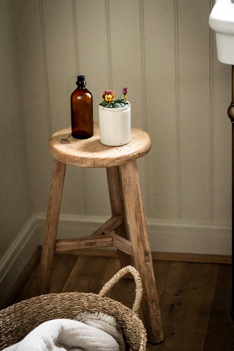 a rustic wooden stool in a serene gentle bathroom carrying an oil bottle and pot plant