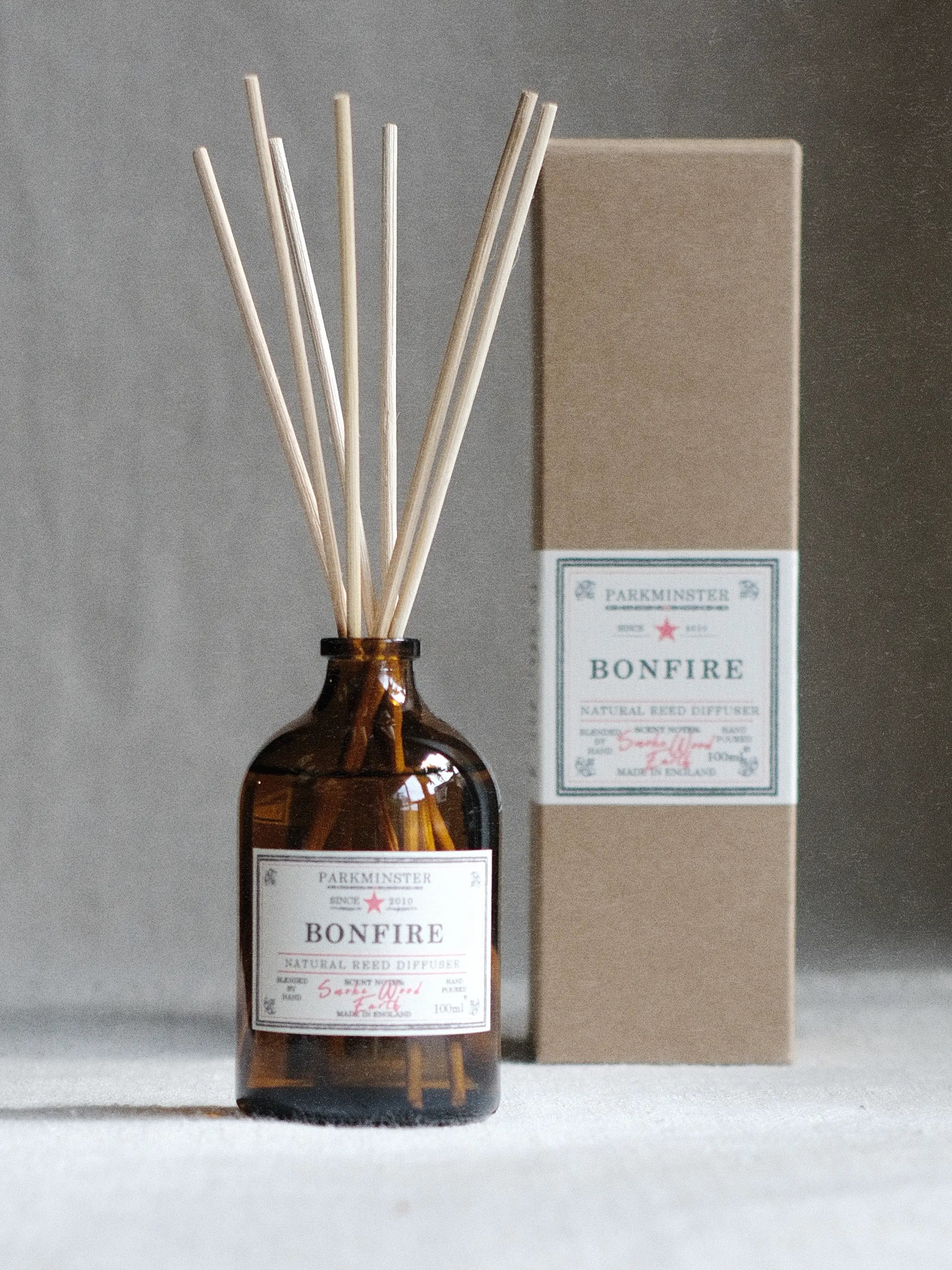 a Woody reed diffuser with smokey wood fragrance, natural plant based home scent in an amber glass bottle by Parkminster