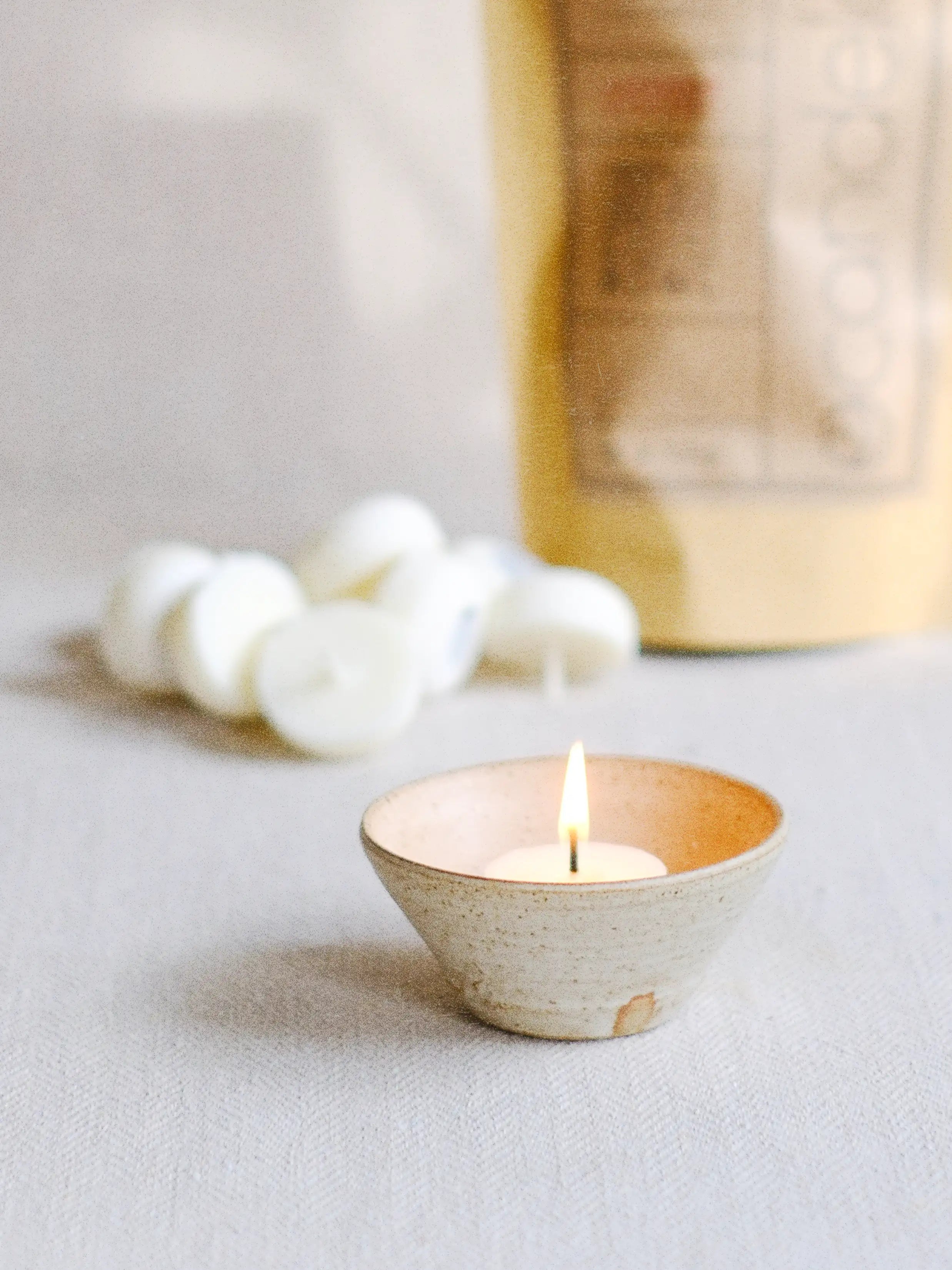 a lit Candela Mini candle made with natural soy wax in a handmade Kneeboneware ceramic bowl