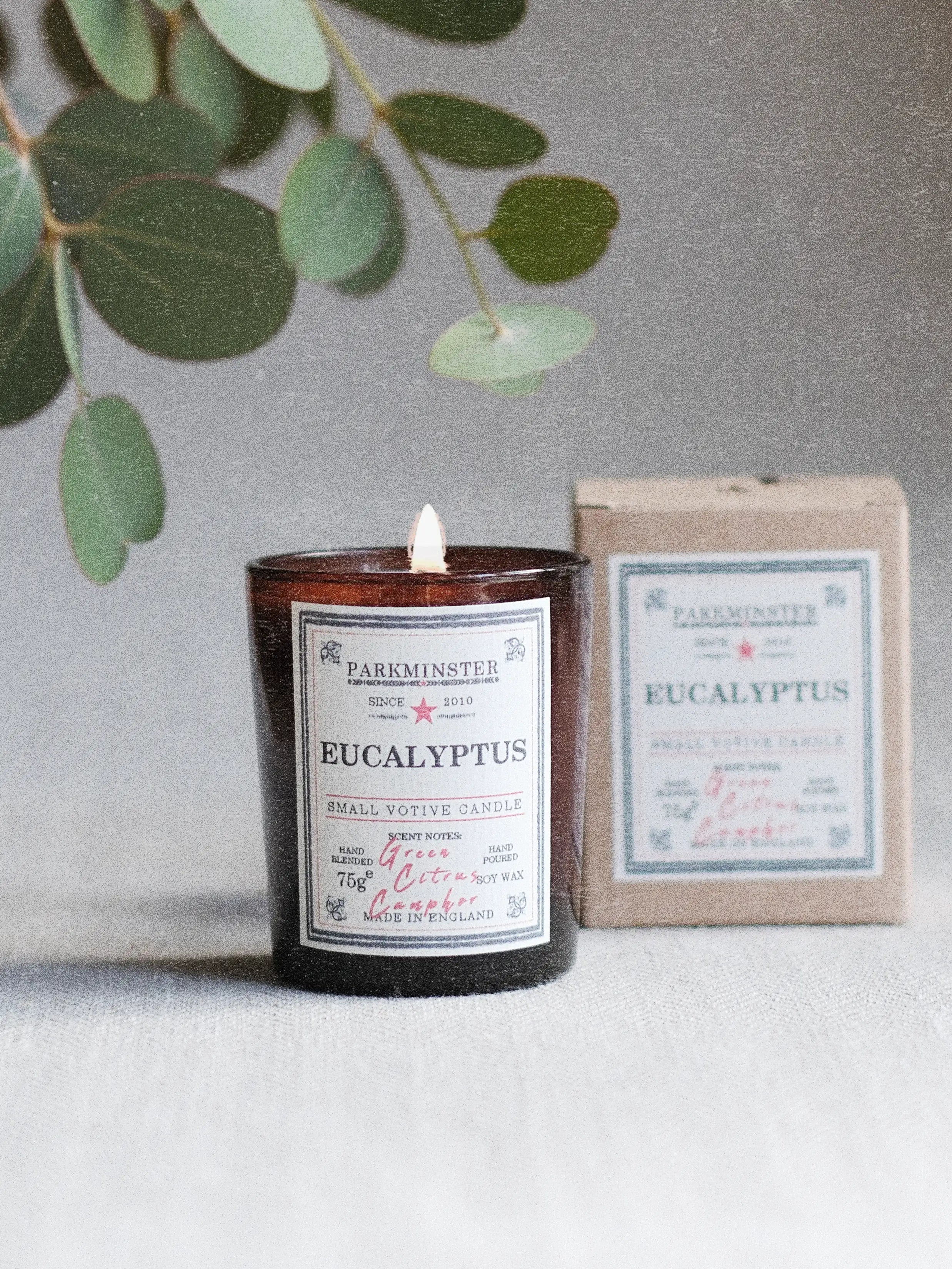 Parkminster Eucalyptus soy wax votive candle made with 100% essential oils, surrounded by fresh eucalyptus leaves for a crisp and calming home fragrance atmosphere