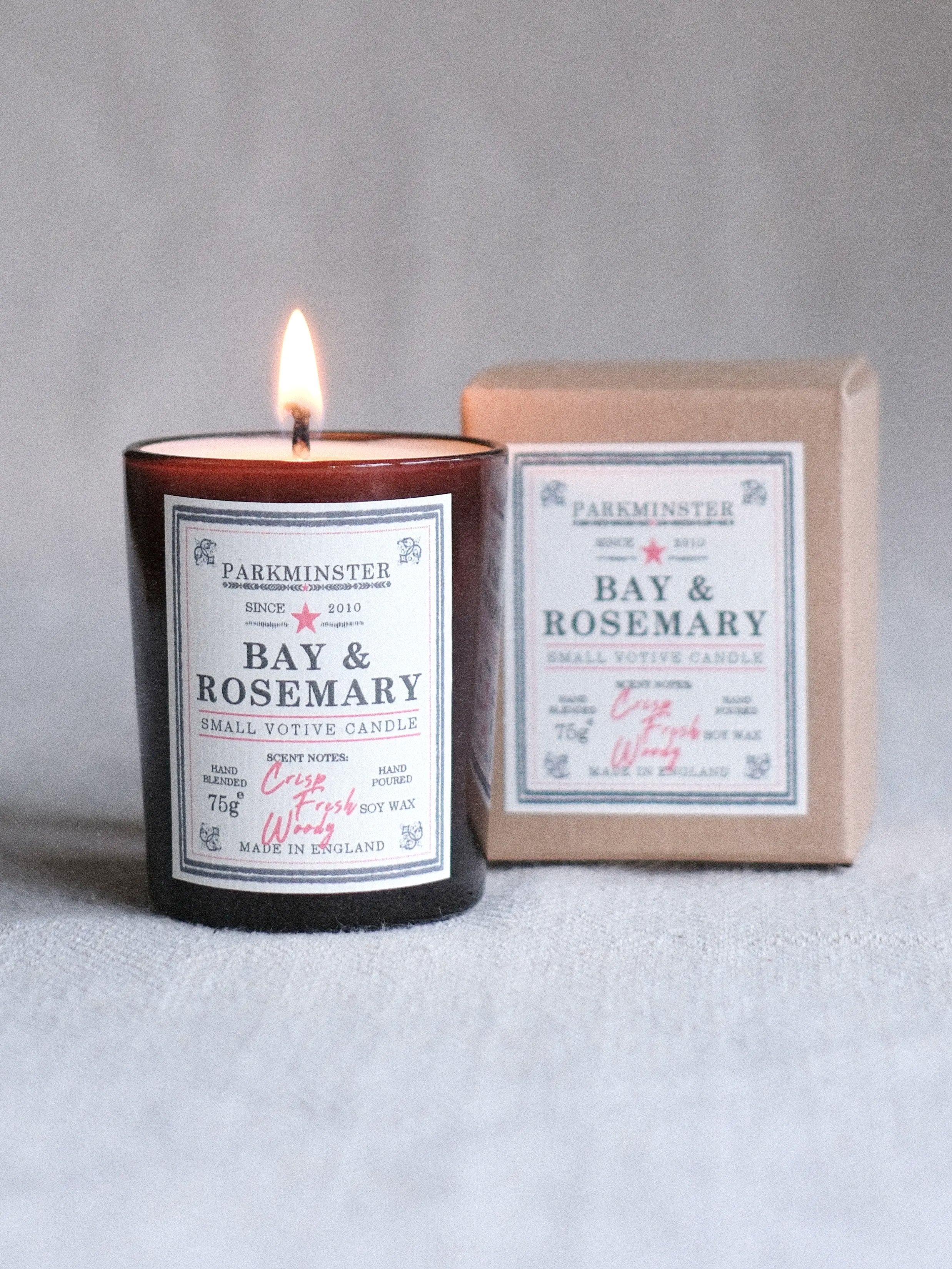 Gently burning Parkminster Bay & Rosemary small votive candle in an amber glass jar with optional kraft paper box