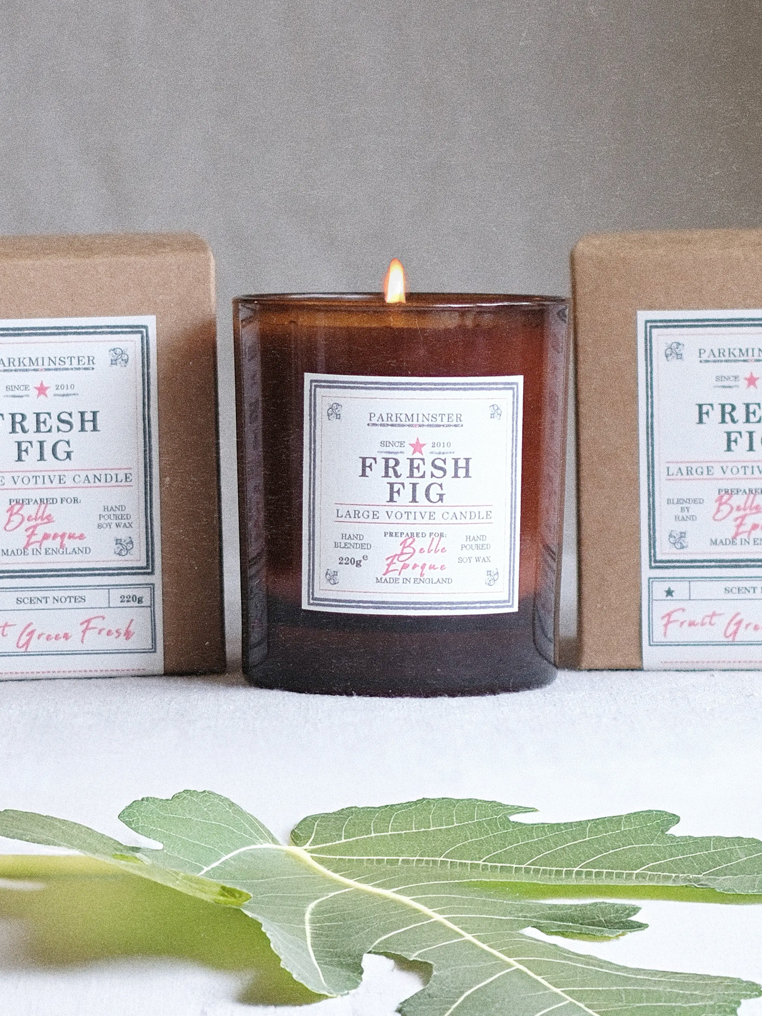 Parkminster Fresh Fig large votive soy candle burning in amber glass jar with recycled kraft box packaging to the side