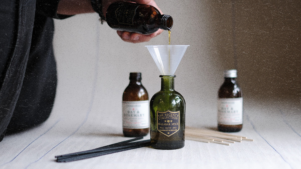 Parkminster reed diffuser refill being poured into an green glass Regency Diffuser bottle with fresh reeds showing how to revive natural home fragrance and restore scent throw in the home