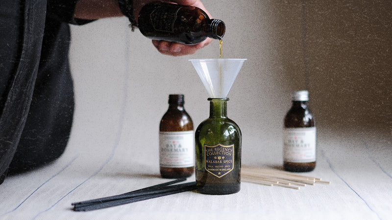 Parkminster reed diffuser refill being poured into an green glass Regency Diffuser bottle with fresh reeds showing how to revive natural home fragrance and restore scent throw in the home