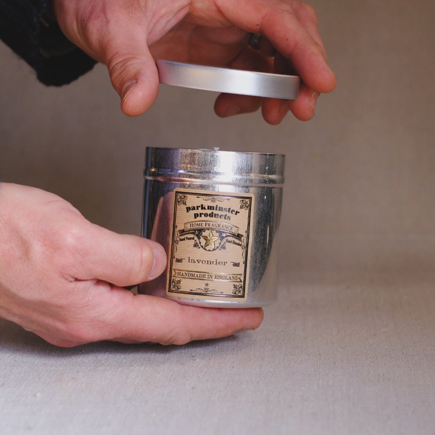 Person removing the lid from a stylish aluminium Lavender Tin Candle, releasing the calming aroma of lavender essential oils for a peaceful and soothing atmosphere.