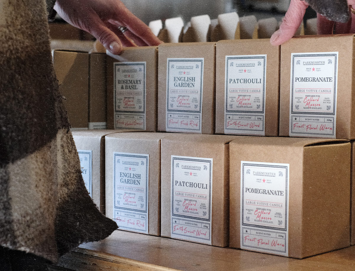 Independent high street shop staff arranging Parkminster large votive soy wax candles on a retail display, showcasing amber glass jars and kraft box packaging