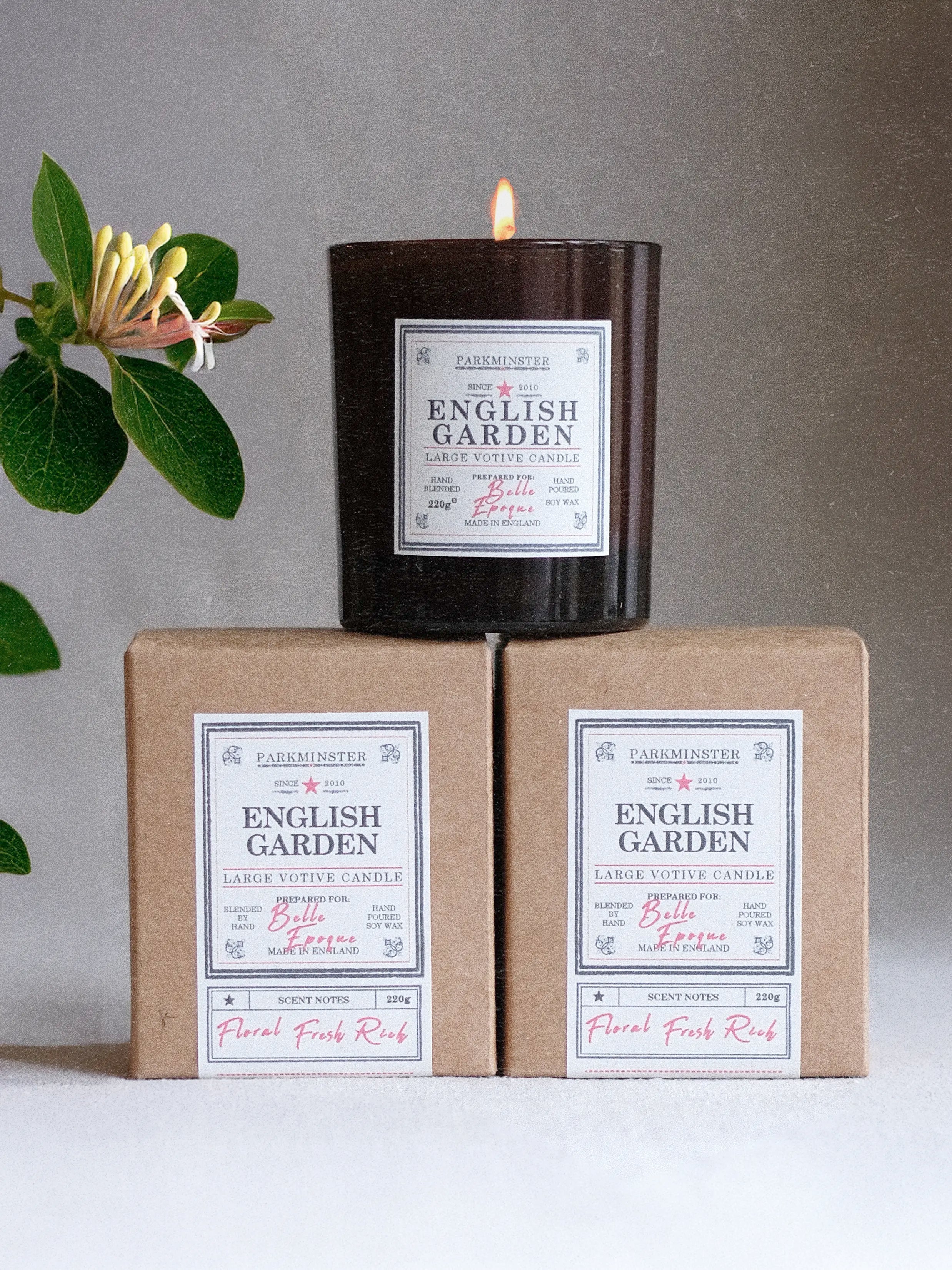 a Parkminster English Garden large votive soy candle alight in an amber glass jar with a recycled kraft box and personalised label option