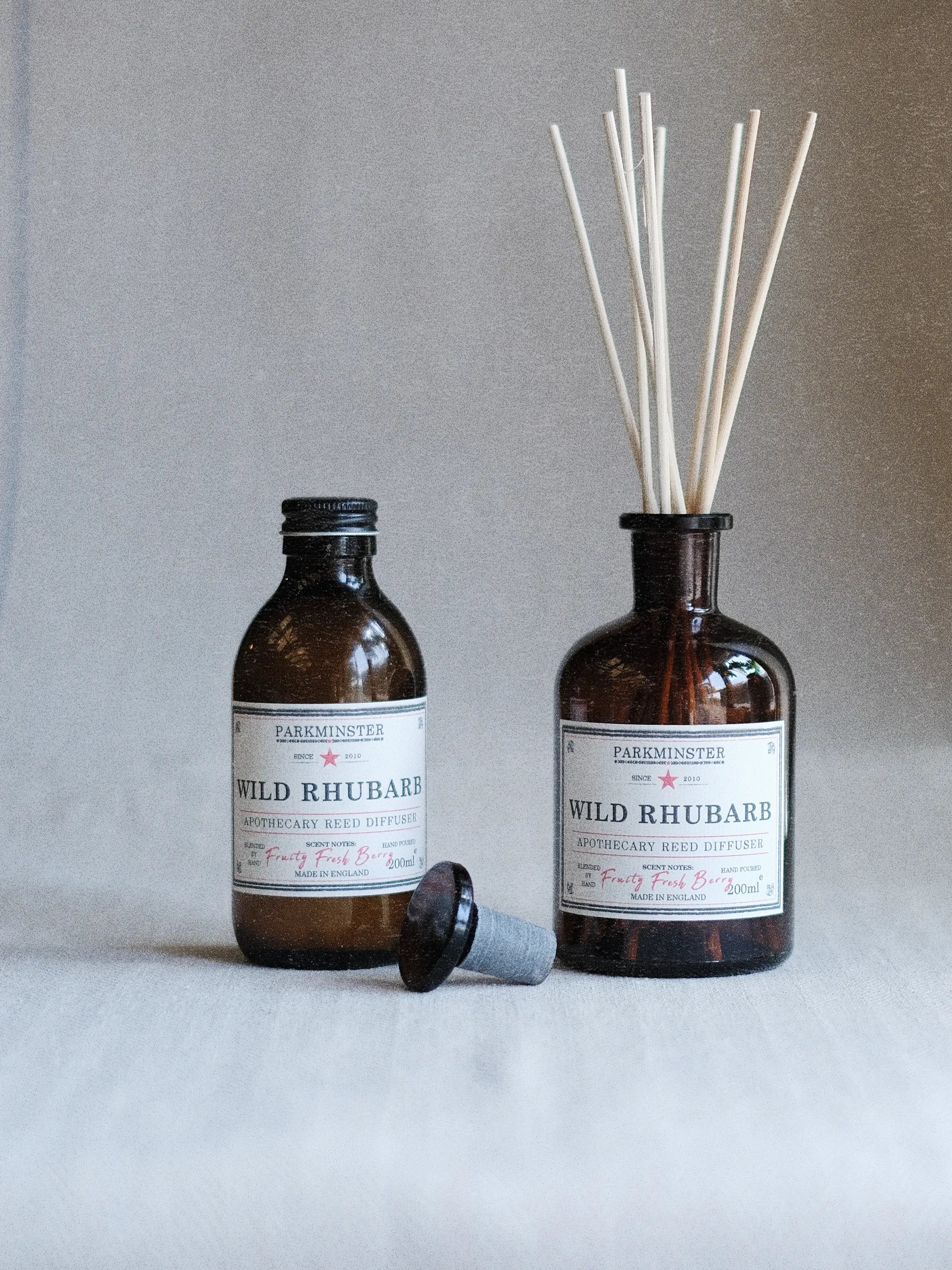 a Parkminster Rhubarb Apothecary Reed Diffuser 200ml amber glass bottle featuring a fruity fragrance with sweet tangy rhubarb notes and natural plant-based home fragrance oils in a modern natural setting